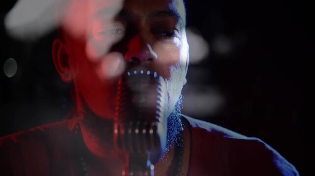 Camera pulling back, male singer leaning into studio mic, revealing face and dog-tag while singing