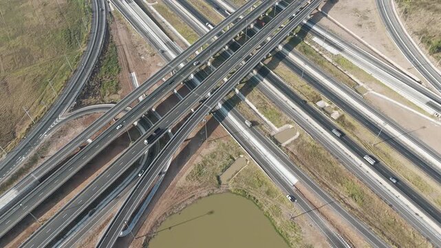 Aerial view of modern highway interchange with multilayer roads and curved ramps surrounded by green farmland, showcasing transportation infrastructure, urban development, and road network planning.