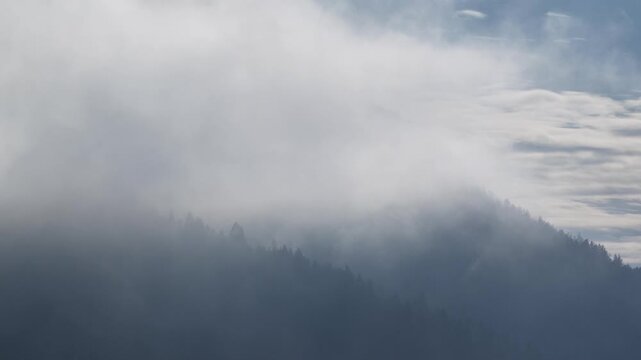 Winter aerial view of alpine village in snowy valley surrounded by mountains and clouds in the Dolomites, Trentino, Italy. Drone shot of snow covered mountain village and valley with rolling clouds