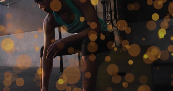Woman placing foot on wrap, adjusting shoe, rubbing ankle, prepping on plyo in gym, bokeh obscuring