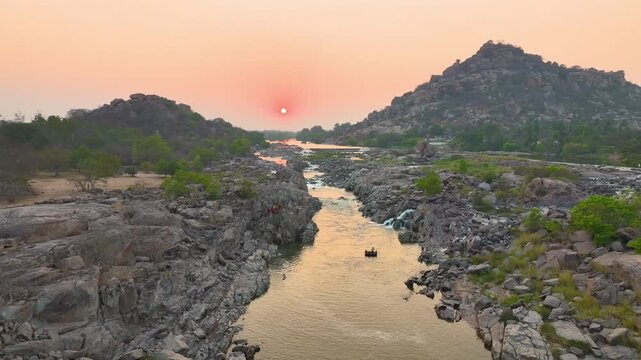 Golden sunset over Tungabhadra River with dramatic boulder formations in Hampi captured by drone.
