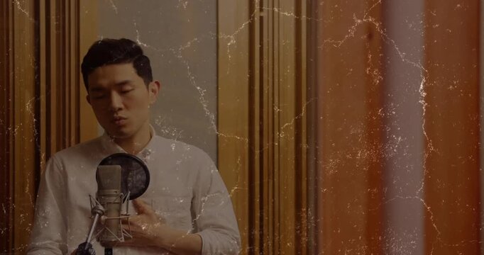 Vertical video: Camera rolling, Asian singer singing into large mic in studio, wearing light shirt