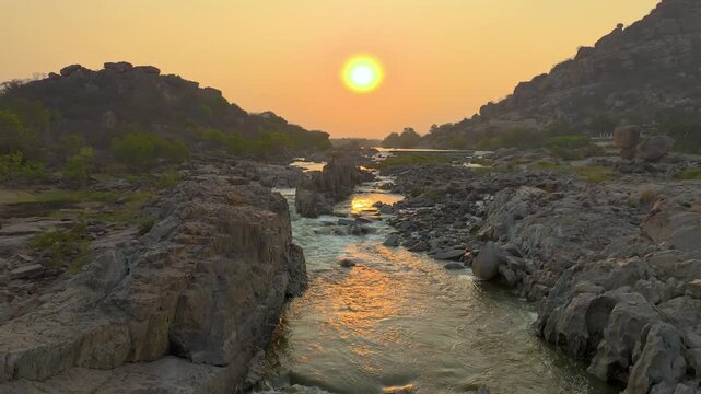 Drone shot of Tungabhadra River winding through ancient boulder landscape during sunset in Hampi.
