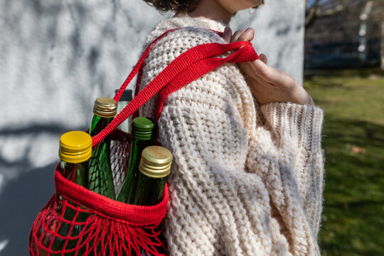 Child carrying glass bottles in reusable net bag outdoors for sustainability
