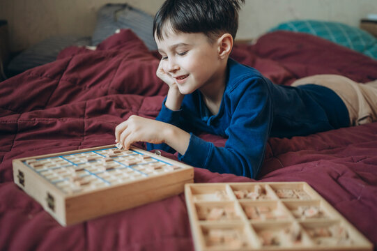 Child playing Sudoku puzzle board game on a bed indoors