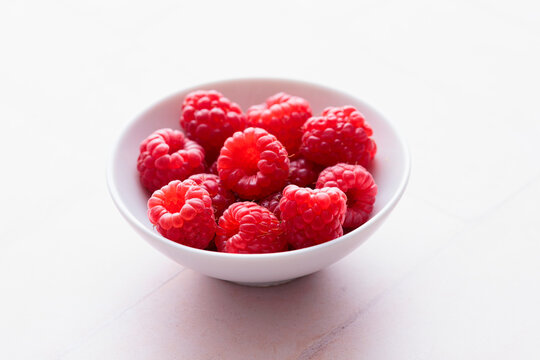 Fresh raspberries in a bowl on tile background in bright studio