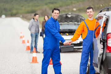 Obraz premium Successful team of professional mechanics standing with arms crossed after providing roadside assistance for a family with a broken car.