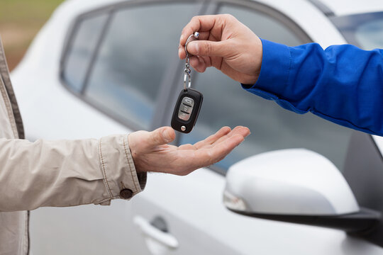 Close-up of a professional mechanic or dealer handing over car keys to a customer in front of a white vehicle.