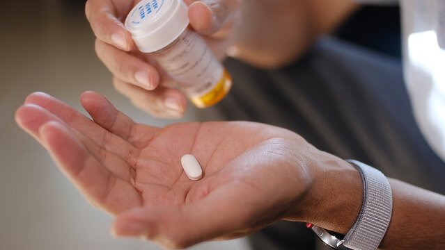 Person holding a single white prescribed pill in an open palm, preparing to take medication from a plastic bottle, managing treatment and health issues
