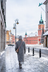 Obraz premium A pedestrian walks down a quiet, snow-covered street in the Old Town, leading the eye toward the Castle Square, Warsaw.