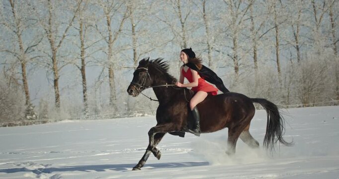Young woman in red dress riding horse in snowy winter forest