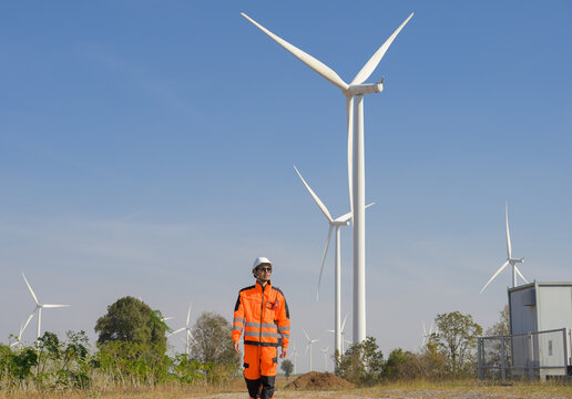 Professional male wind farm technician in safety uniform inspecting renewable energy turbines at wind power plant