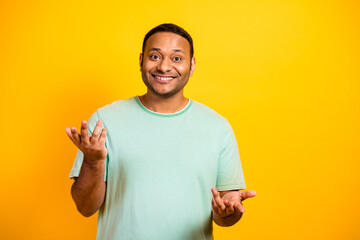 Happy mixed man in a casual mint t shirt smiles and gestures against a bright yellow background for...