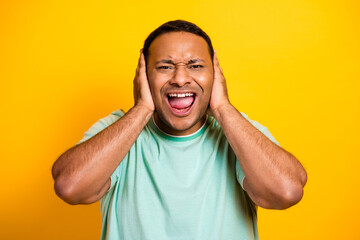 Happy man shouts with hands on ears against yellow background wearing mint green tshirt for...
