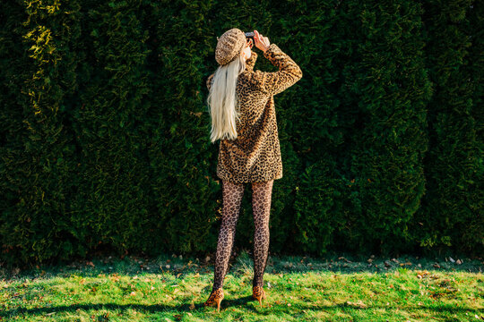 Stylish person in leopard jacket taking photographs in garden outdoors