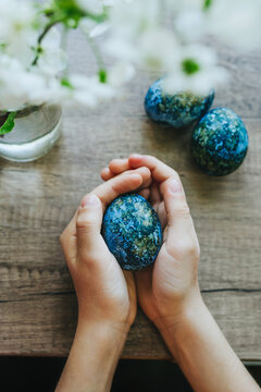 Girl holding dyed Easter egg with natural color on wooden table