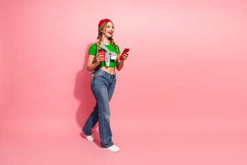 Young stylish woman in green top with pink background holding phone and coffee smiling