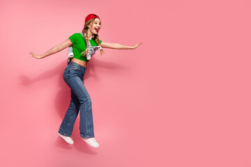 Young stylish girl in green crop top jeans and cap posing playfully against pink background