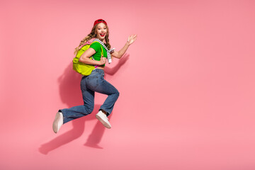 Naklejka premium Young hipster girl with bright green backpack jumps in the air smiling against pink background