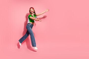 Young woman jumping with joy in pink background wearing jeans green top cap and sneakers