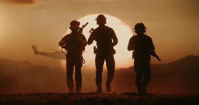 Three Armed Soldiers in Silhouette Walk Across Desert at Sunset While a Helicopter Flying in Background. Patrol During a Mission, Active Warfare, Conflict, Military Operation. Slow Motion Cinematic