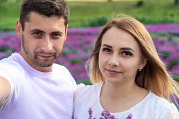 Fototapeta premium Happy young couple taking a selfie on a smartphone in a lavender field.