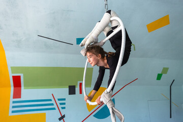 Girl doing strength tricks on aerial hoop, safe acrobatic routine, protected with elastic foot wraps, child circus training. © Ольга Симонова