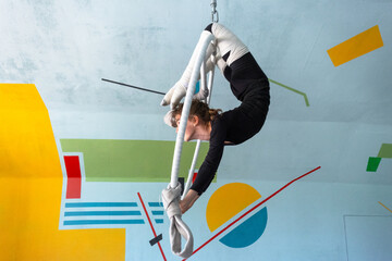 Girl performing acrobatic tricks on aerial hoop, elastic bandages for leg safety, gym background, focused circus athlete. © Ольга Симонова