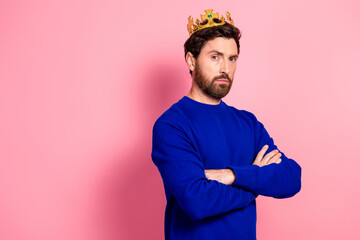 Confident young man with crown wearing blue sweater stands against pink background for royalty inspired fashion stock photo suitable for advertising and lifestyle campaigns © deagreez