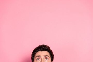 Young man looks up with curiosity against pink background wearing a blue sweater