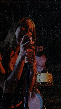 Female lead vocalist bringing mic close and singing in live music, animated grain boosting emotion