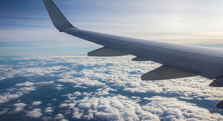 Obraz premium Aerial view shows a plane wing above cumulus cloudscape against a blue sky, conveying travel, flight, and adventure, above the cloud layer