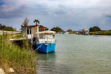Traditional fishing boats moored in river mouth by rustic huts near Mediterranean coast. Calm water landscape under cloudy sky. G&uuml;ndoğdu, Manavgat, Antalya, Turkey.