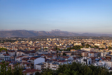 Fototapeta premium Panoramic view of Manavgat city at golden hour before sunset. Dense residential buildings with solar panels on roofs against majestic Taurus mountains. Antalya region, Turkey.