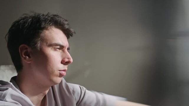 Handheld chest up shot of unmotivated male Caucasian zoomer sitting in morning bedroom with cup of coffee, lost in thought
