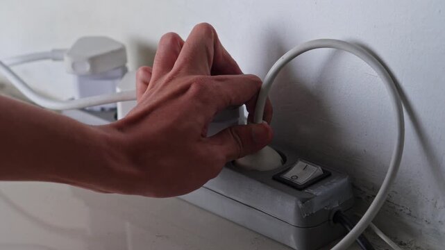 Close-up of hand disconnecting multiple plugs from power strip to reduce standby consumption