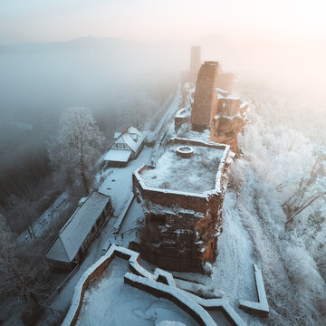 Aerial view of the weathered Dahn Castle ruins, a stark contrast against the snowy landscape and ethereal fog, Dahn, Rheinland-Pfalz, Germany.