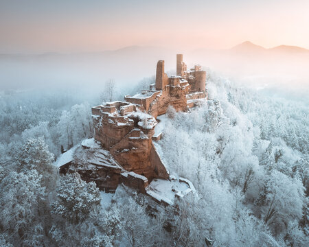 Aerial view of the frosted Burgruine Altdahn castle ruins perched atop a snow-laden hill, kissed by the soft glow of dawn, Dahn, Rheinland-Pfalz, Germany.