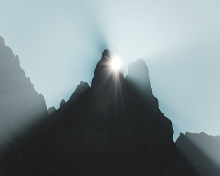 View of stark, shadowy peaks contrast against the ethereal glow of the sun, a celestial dance of light and form in the mountains, Trentino-Alto Adige, Italy.