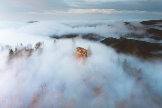 Aerial view of a sandstone rock formation piercing through a dense, ethereal fog, like a lost island rising from a sea of clouds, Wingen, Grand Est, France.