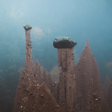 View of submerged earth pyramids rise eerily from the lakebed, capped with dark stones against the muted blue water, in Trentino-Alto Adige, Italy.