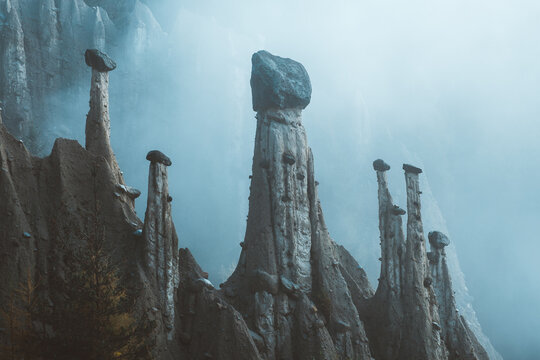 View of earth pyramids rise dramatically from the landscape, each capped with a protective stone under a hazy sky, Segonzano, Trentino-Alto Adige, Italy.