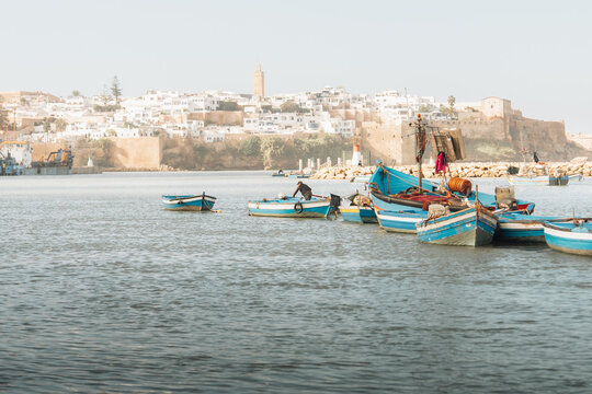 View of vibrant blue fishing boats bob gently on the shimmering water against the backdrop of the ancient city walls, Rabat, Rabat-Sale-Kenitra, Morocco.