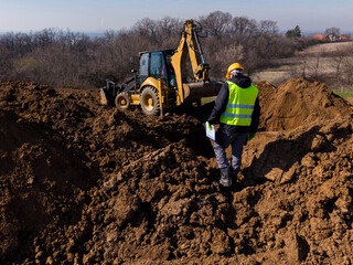 Construction engineer supervising backhoe excavation on earthworks site