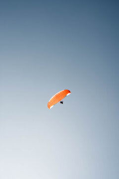 View of a lone orange paraglider soars against the clear blue sky, offering a vivid contrast and sense of freedom, Interlaken, Switzerland.