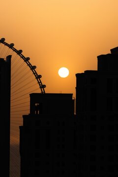 View of silhouetted buildings and Ain Dubai Ferris wheel under a blazing sunset sky, Dubai, United Arab Emirates.