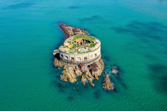 Aerial view of Stack Rock Fort, a haunting ruin stands defiant against the teal sea, its weather-beaten stone whispering tales of maritime history, Wales, United Kingdom.