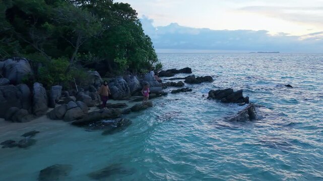 Aerial view of Tanjung Gelam Beach, where turquoise waters meet the sandy shore, framed by lush greenery and people enjoying the coastal beauty, Karimunjawa, Central Java, Indonesia.
