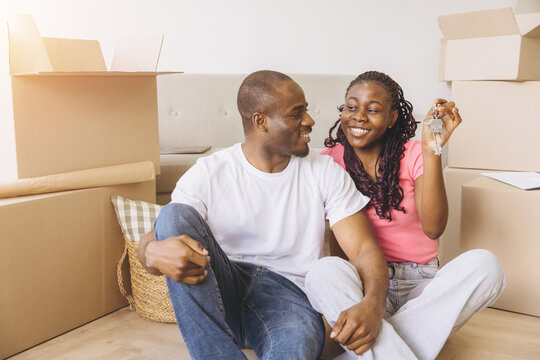 Young black couple smiling, holding keys to their new house. Celebrating moving day and future home ownership together