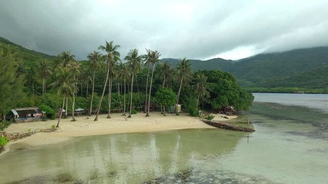 Aerial view of Bobby Beach showcasing the serene bay, golden sand, and lush green palm trees against the cloudy sky, Karimunjawa, Jawa Tengah, Indonesia.